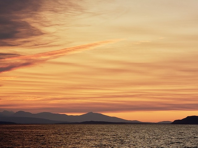 An orange and pink sunset over the Strait of Georgia, with the mainland mountains in silhouette across the water.